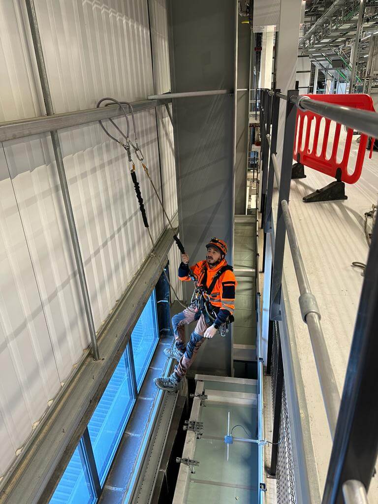 A man in an orange vest is climbing a ladder on a building facade.