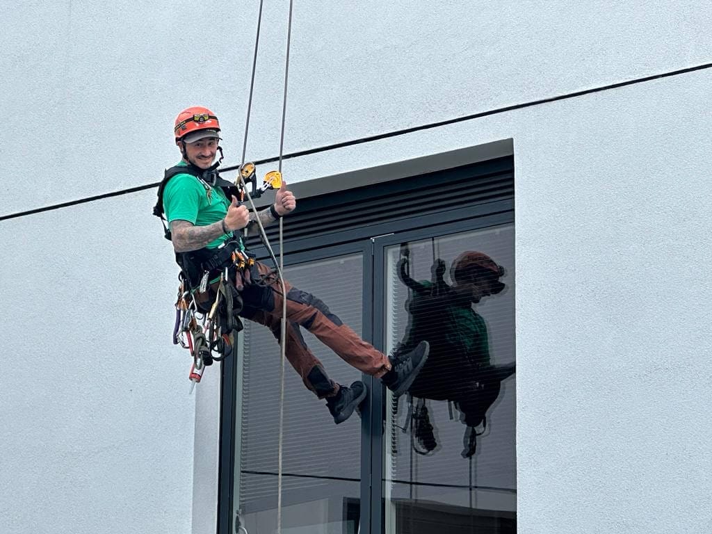 A man offering services hangs precariously from a window on a rope.