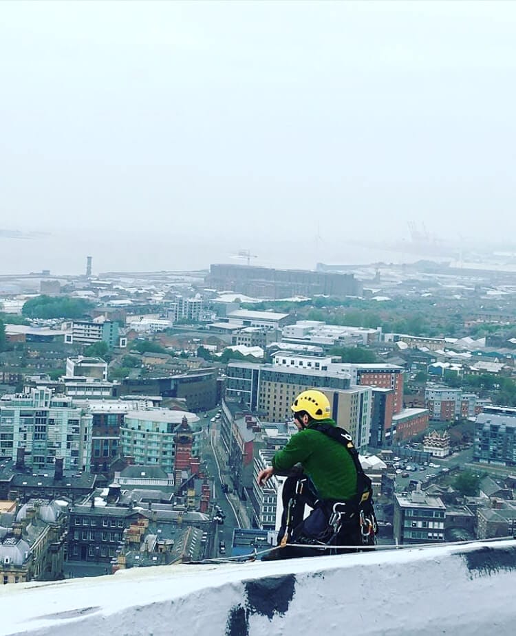 A man riding a bike on a ledge overlooking a city, showcasing the architectural and building maintenance marvels.