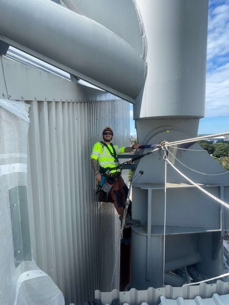 A man is performing building maintenance by climbing up the side of a wind turbine.