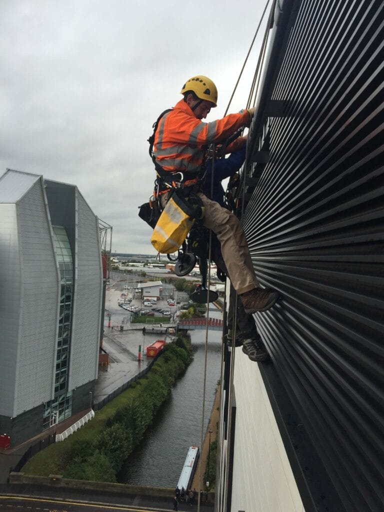 A worker is hanging from a building on a rope while providing services.