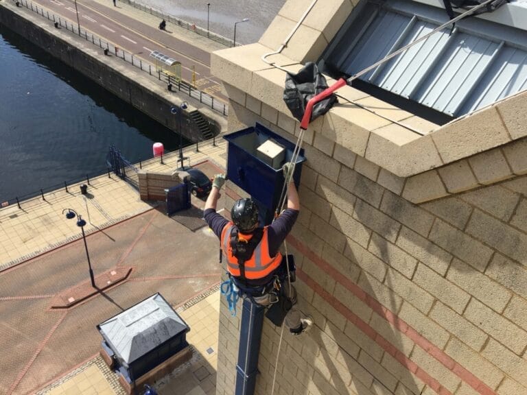 A painting worker on a ladder on the side of a building.