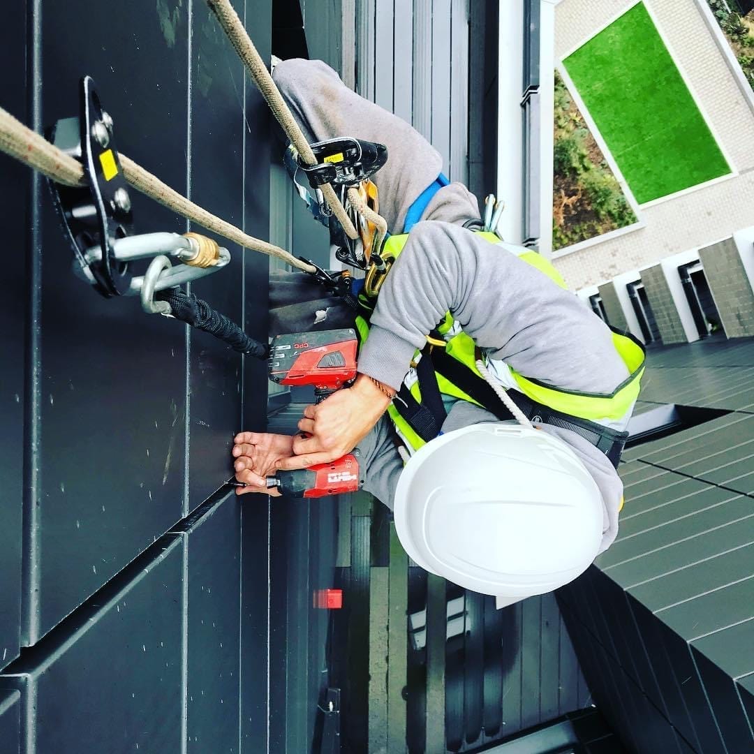 A _rope access_ construction worker is working on a roof.