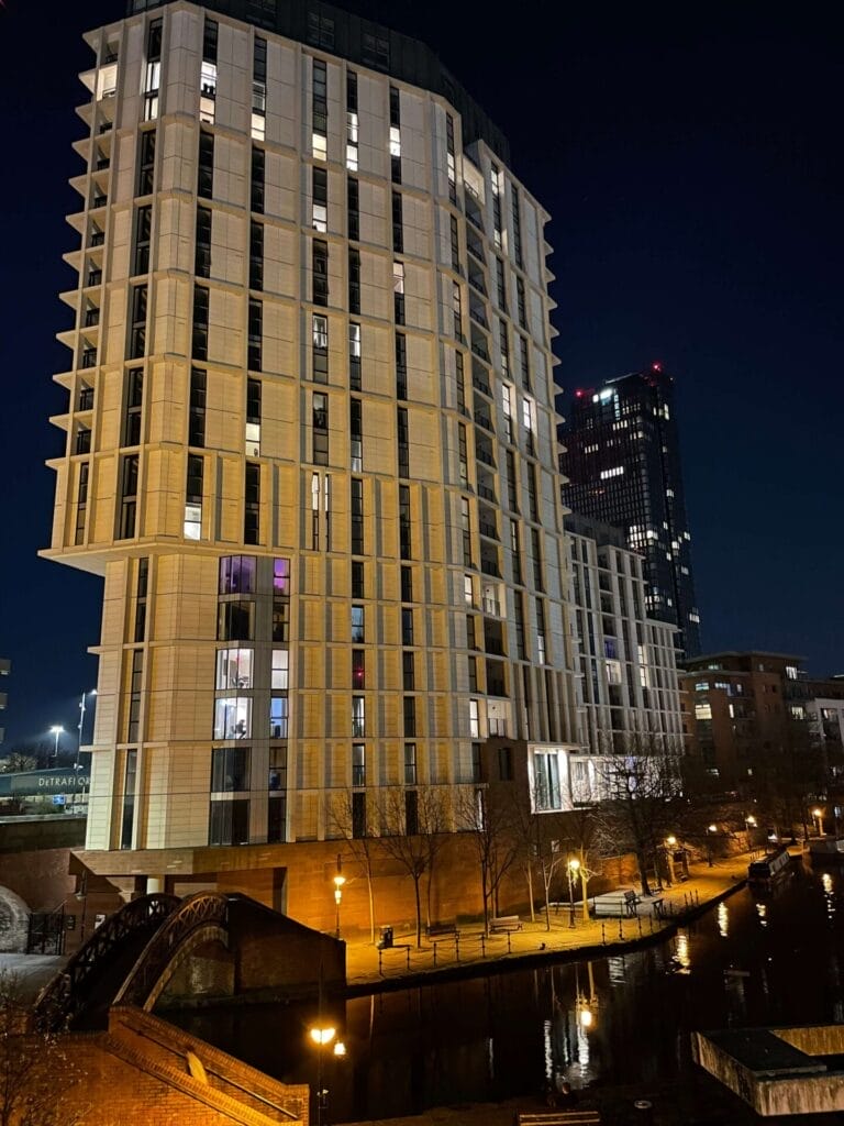 A large building near a canal is beautifully illuminated at night, showcasing its architectural grandeur while hinting at the meticulous building maintenance.