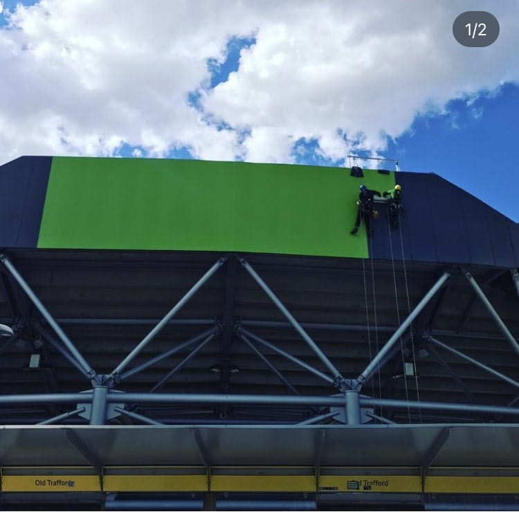 A man is installing a large green banner on the side of a building.