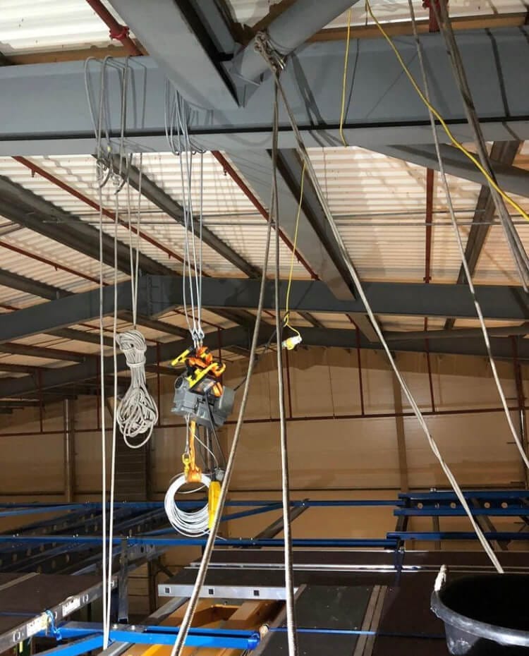 An electrician installing ropes hanging from the ceiling of an industrial building.