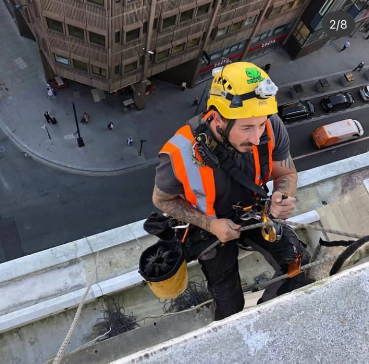 A man is providing services on a ledge of a building.
