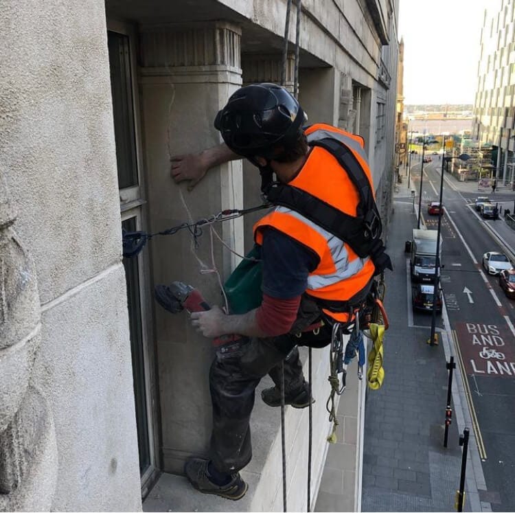 A man is climbing a window in a city, demonstrating a daring act that challenges the boundaries of urban heritage conservation.
