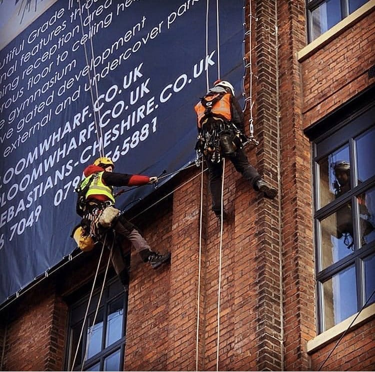 Two construction workers on the side of a building, working on the installation.