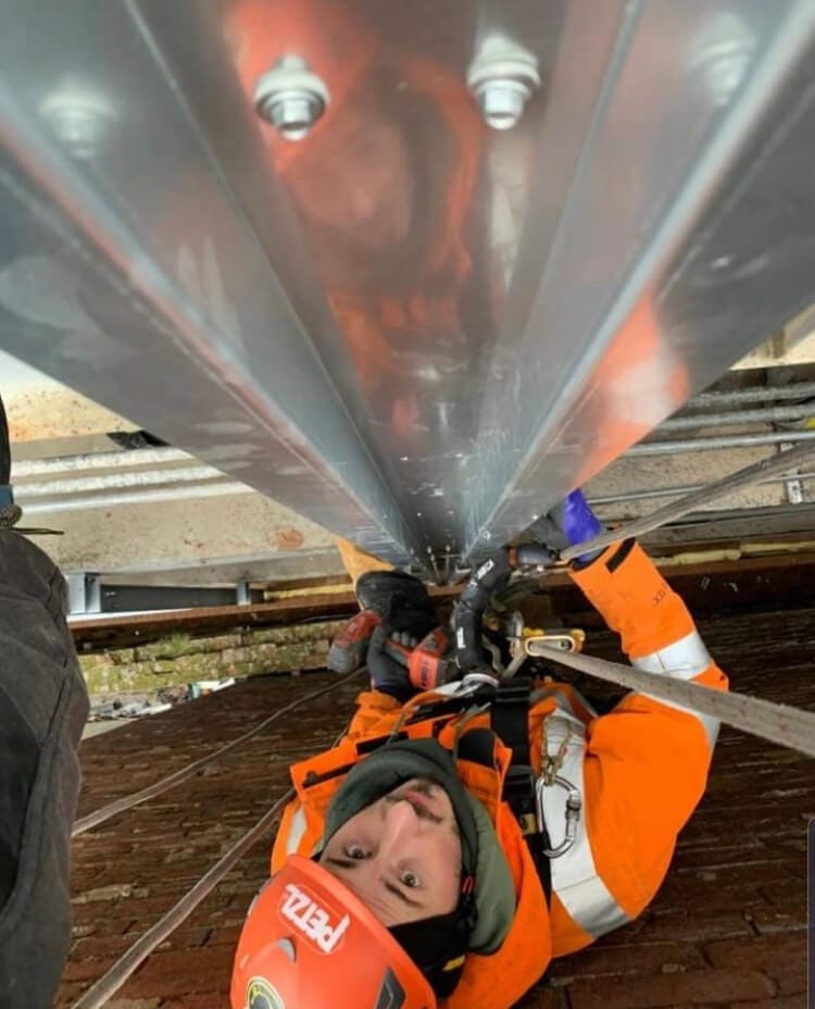 A man in an orange jacket is working on a metal facade.