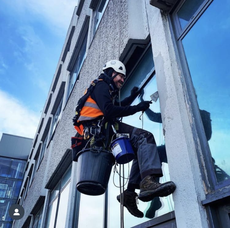 A rope access specialist from Manchester diligently cleaning the windows of a building.