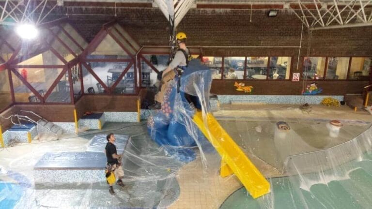 A man is painting a water slide in an indoor pool.