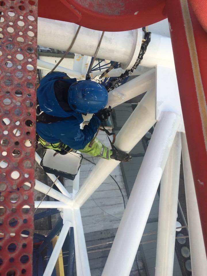 A worker is painting on the top of a large structure.