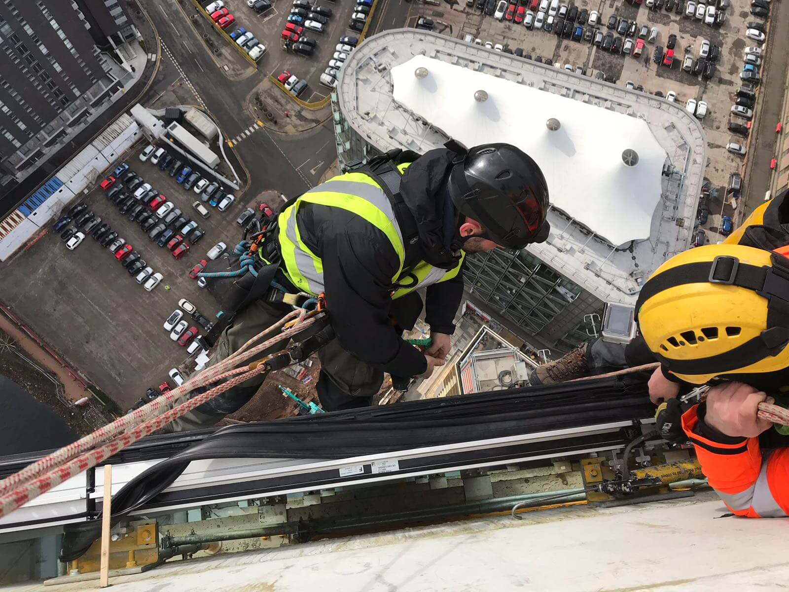 Two men working on the edge of a building, repairing glass.