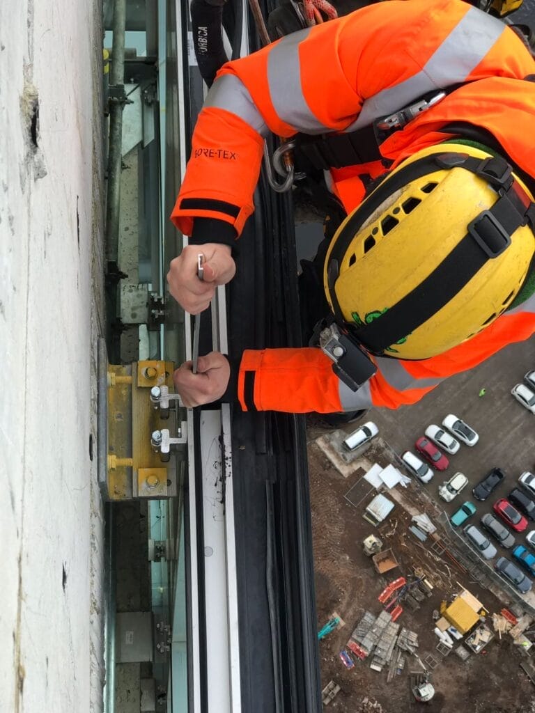 A man in an orange vest is performing glass repair on a window.